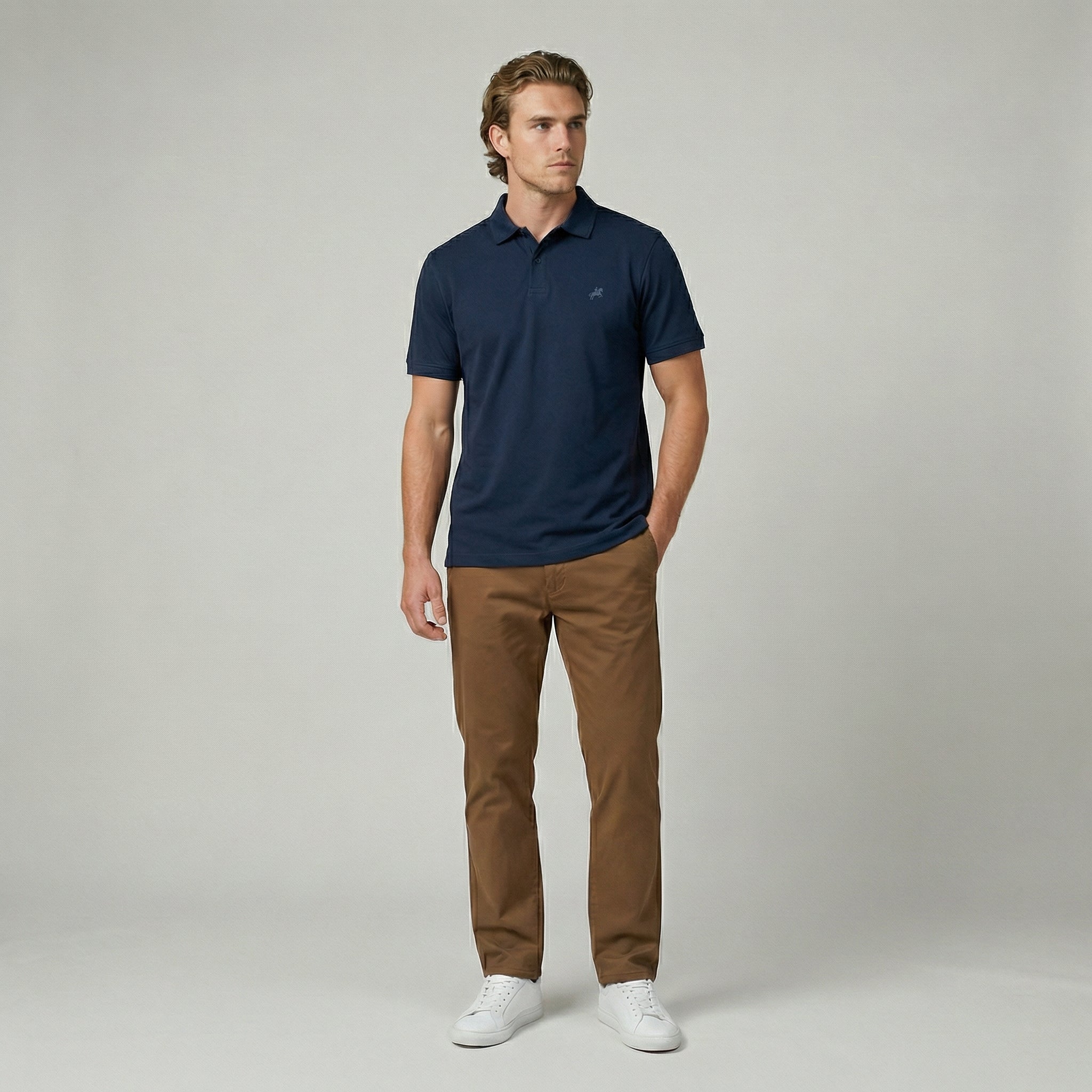 Man wearing a navy polo shirt and brown pants on a gray background