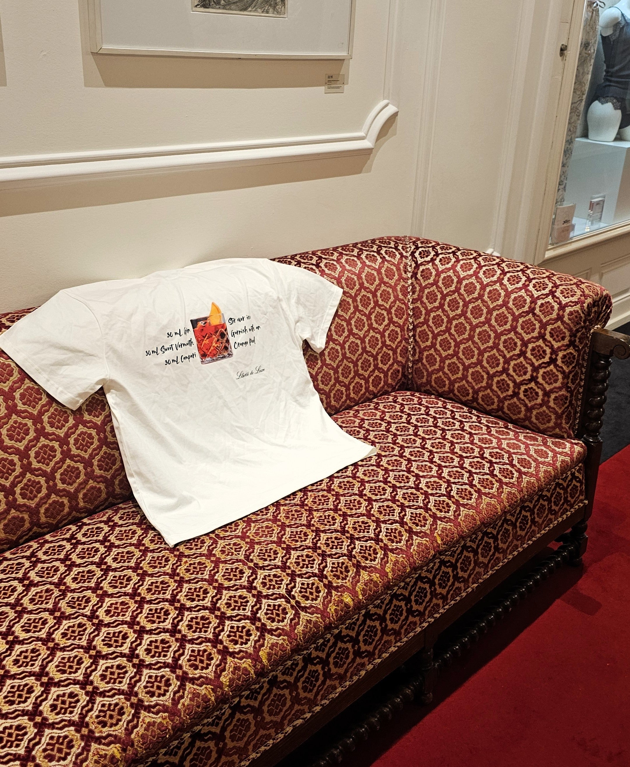 White t-shirt with text and graphics on a patterned red sofa