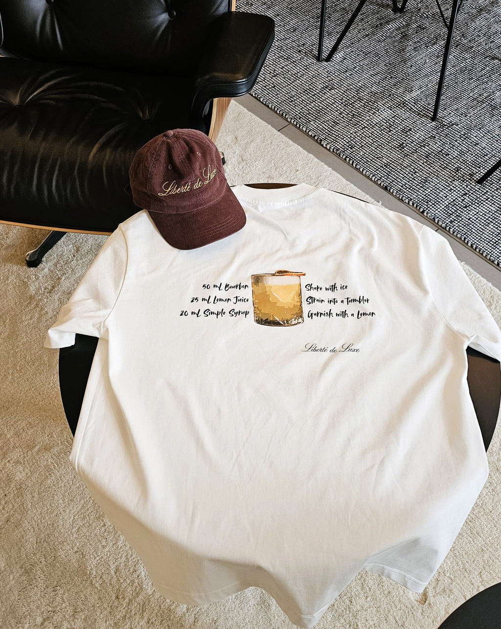 White t-shirt with graphic design and text on a chair, with a brown cap on top.