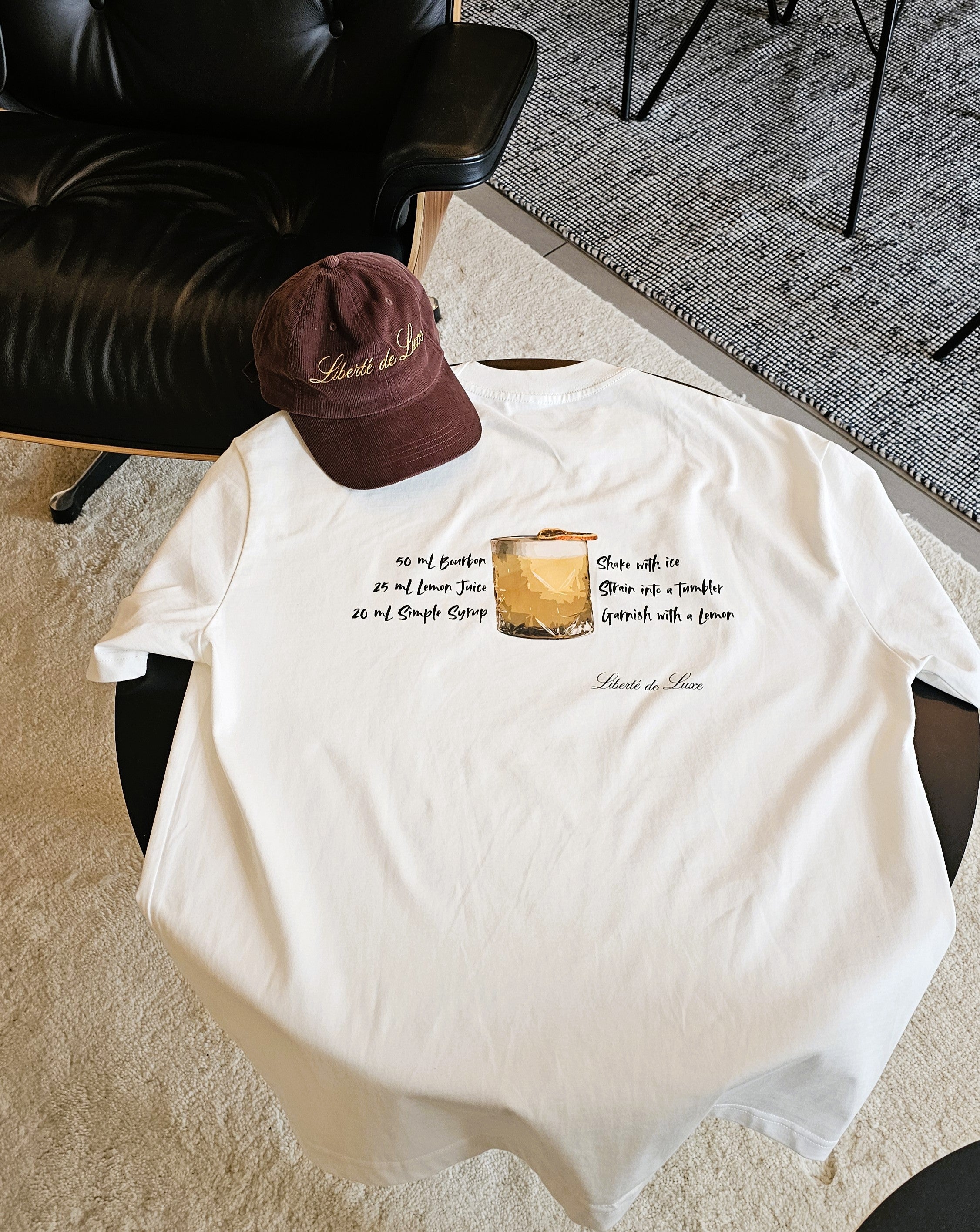White t-shirt with graphic design and text on a chair, with a brown cap on top.