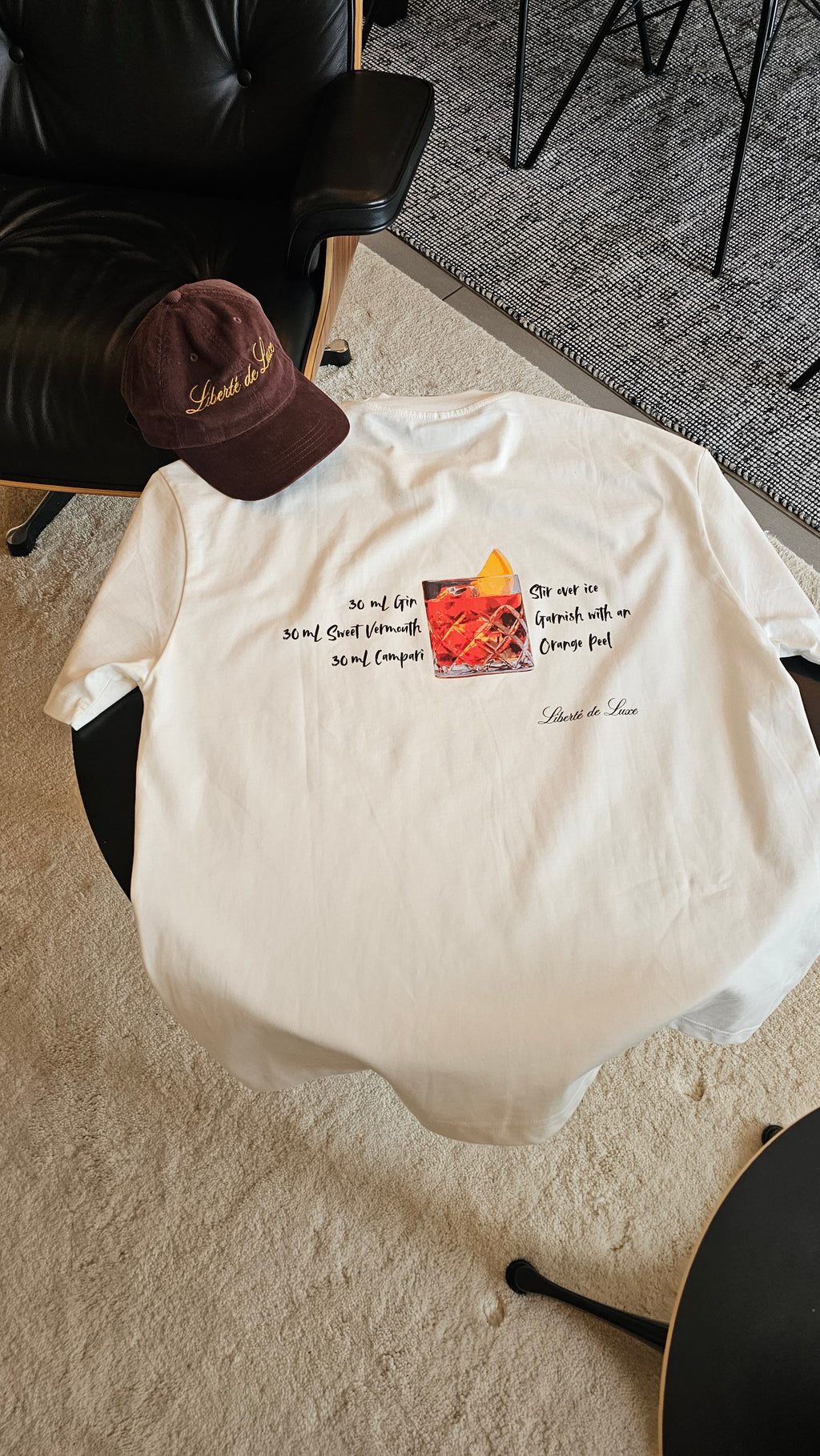 White t-shirt with a colorful graphic and text on a gray floor.