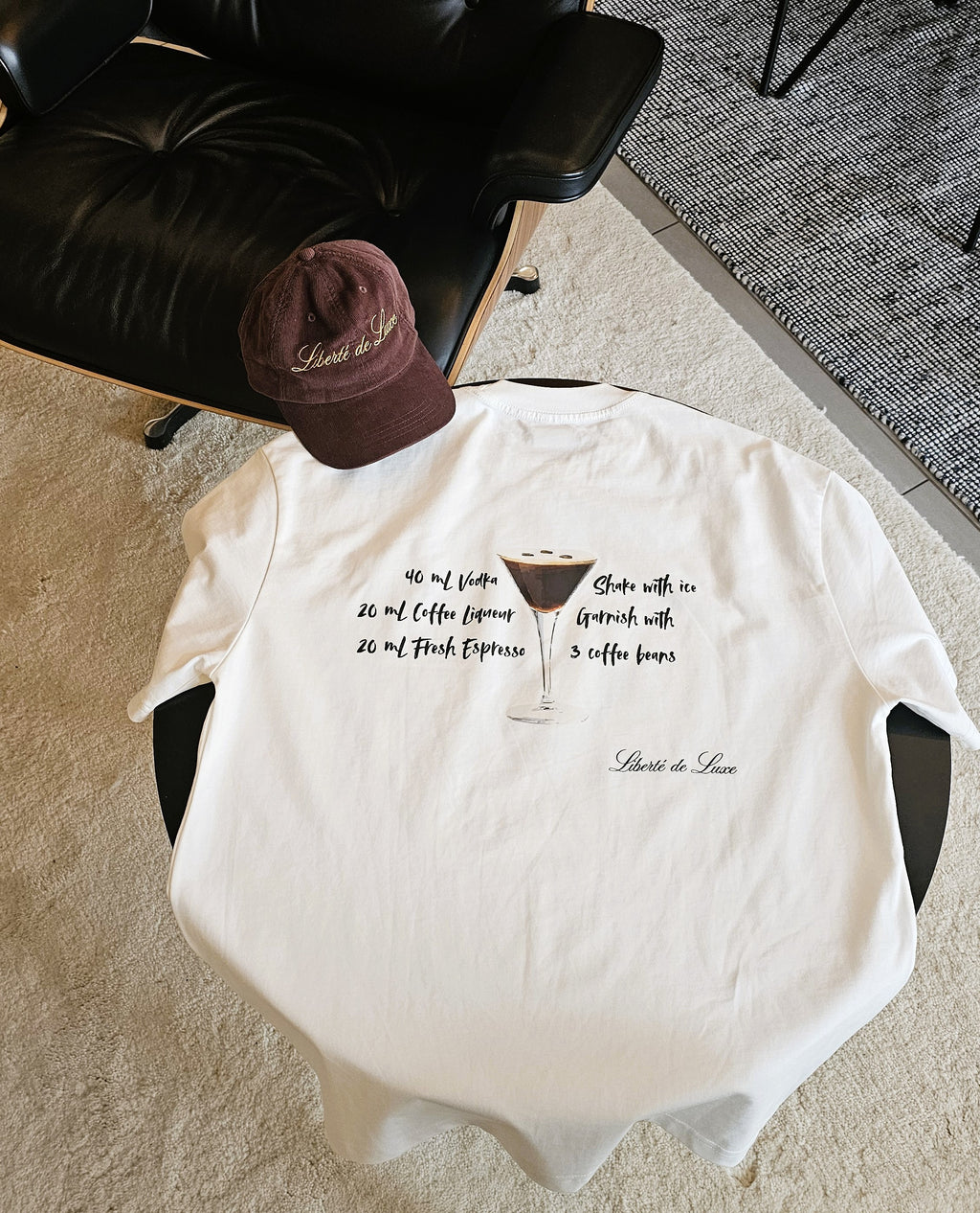 White t-shirt with text design on a chair, accompanied by a brown cap.