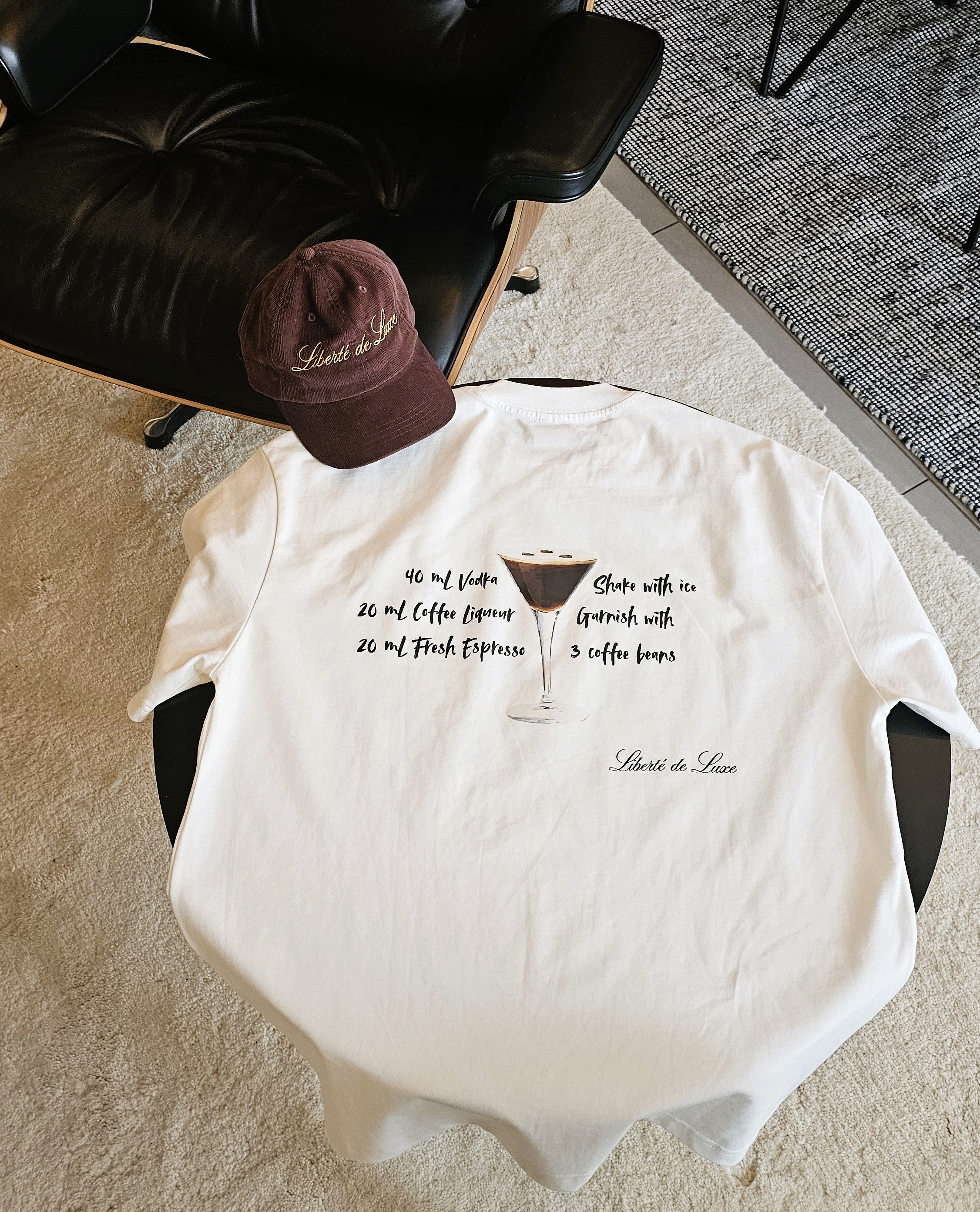 White t-shirt with text design on a chair, accompanied by a brown cap.
