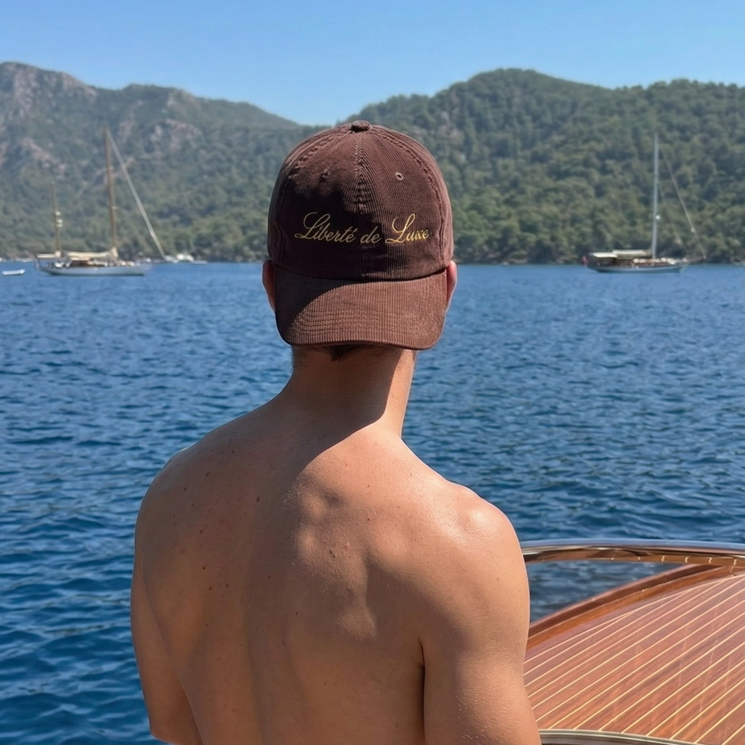 Man on a boat wearing a cap with a scenic background of mountains and water.