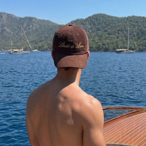 Man on a boat wearing a cap with a scenic background of mountains and water.